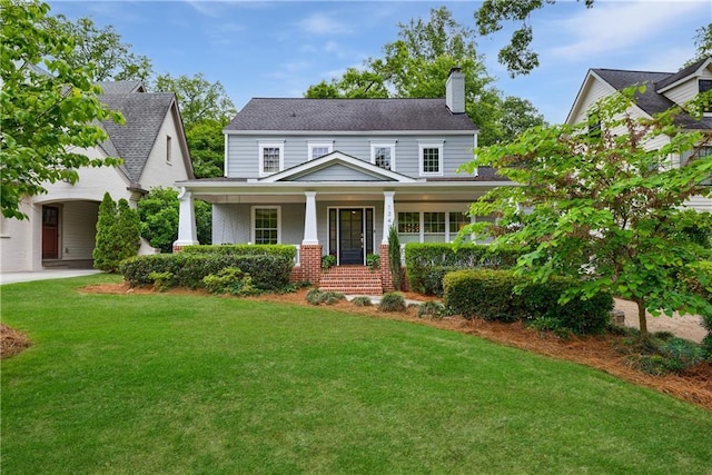 view of front facade with a chimney, roof with shingles, a front lawn, a porch, and brick siding