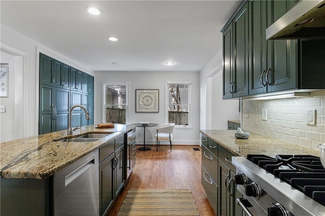kitchen featuring light stone counters, tasteful backsplash, a sink, appliances with stainless steel finishes, and under cabinet range hood
