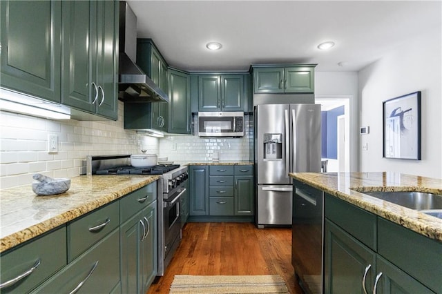 kitchen with green cabinetry, dark wood-style floors, appliances with stainless steel finishes, and wall chimney range hood