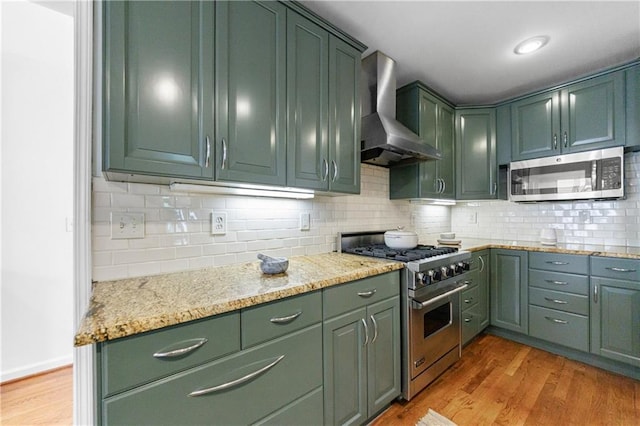 kitchen with wall chimney range hood, green cabinetry, stainless steel appliances, and light wood-style flooring