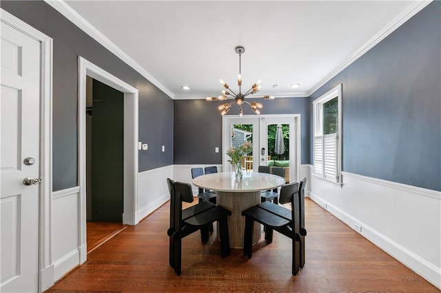 dining room featuring crown molding, a chandelier, a wainscoted wall, dark wood-style floors, and french doors