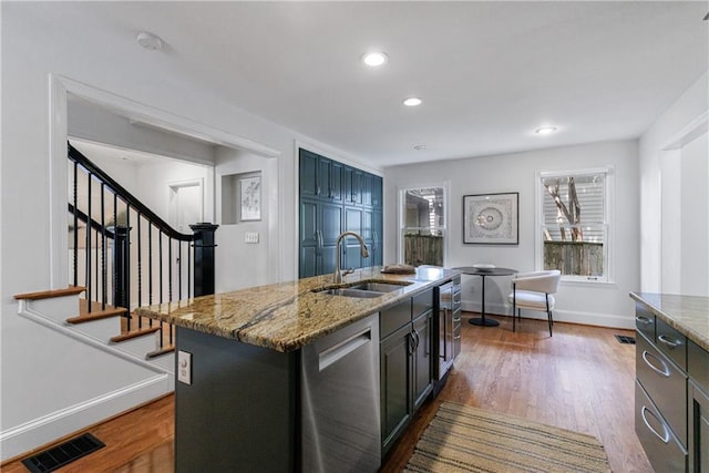 kitchen featuring stainless steel dishwasher, a sink, visible vents, dark wood-style flooring, and light stone countertops