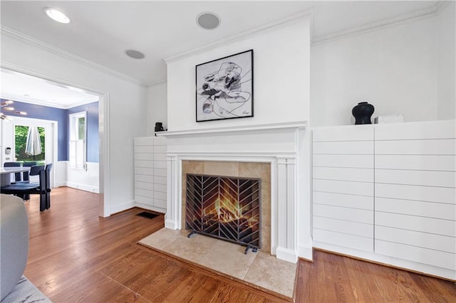 unfurnished living room featuring a tiled fireplace, crown molding, visible vents, baseboards, and wood finished floors