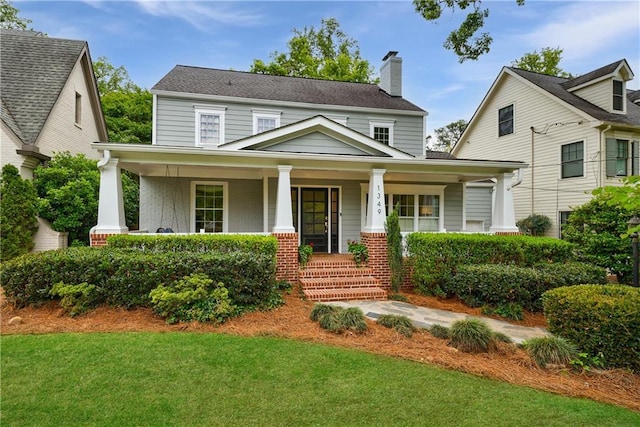 view of front of home with a front yard, a chimney, a porch, and brick siding