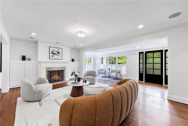 living room with recessed lighting, wood finished floors, a tile fireplace, baseboards, and crown molding