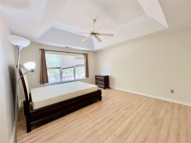 bedroom featuring ceiling fan, light wood-type flooring, and a tray ceiling