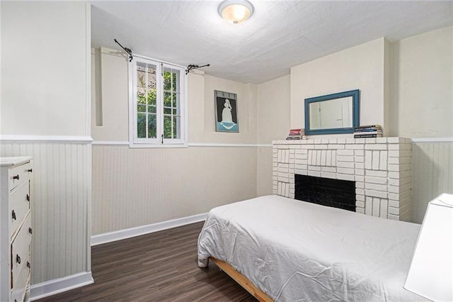 bedroom featuring a wainscoted wall, a fireplace, baseboards, and wood finished floors