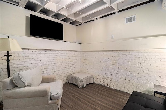 living room with brick wall, visible vents, and wood finished floors