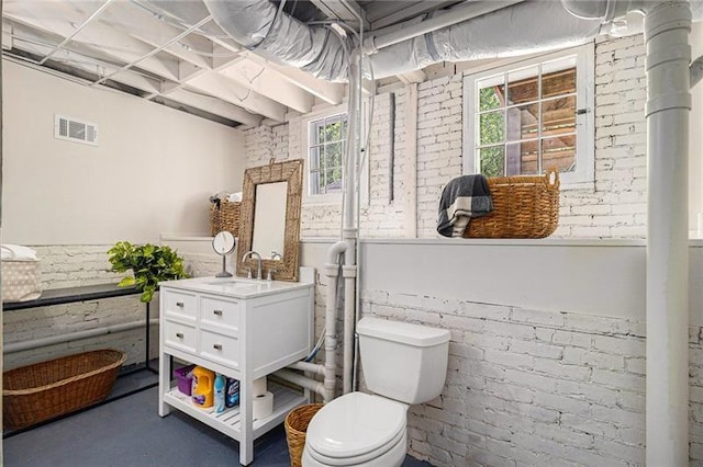 bathroom with visible vents, toilet, a wainscoted wall, brick wall, and vanity