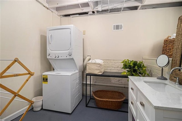 laundry area with stacked washer and dryer, cabinet space, a sink, and visible vents