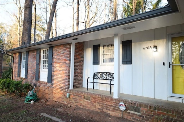 property entrance with board and batten siding, brick siding, and covered porch