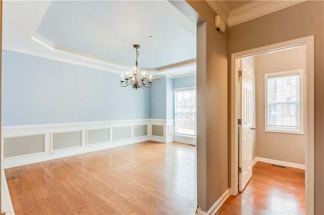 interior space featuring a raised ceiling, crown molding, a chandelier, and light wood-type flooring