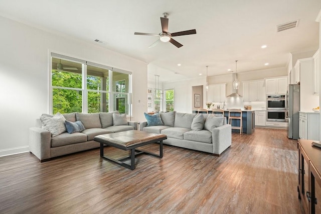 living room featuring a ceiling fan, visible vents, ornamental molding, and wood finished floors
