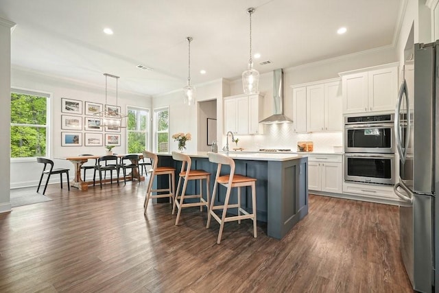 kitchen featuring wall chimney exhaust hood, white cabinets, a wealth of natural light, and stainless steel appliances