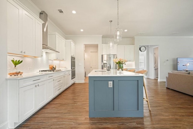 kitchen featuring crown molding, appliances with stainless steel finishes, an island with sink, wall chimney exhaust hood, and tasteful backsplash