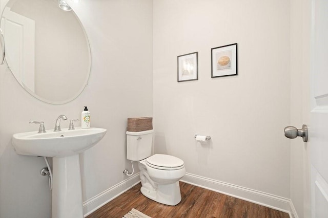 half bath with baseboards, toilet, and wood finished floors