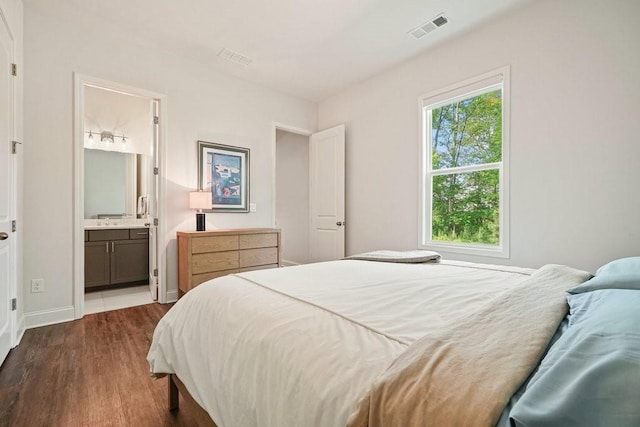 bedroom featuring dark wood-style flooring, visible vents, a sink, baseboards, and connected bathroom