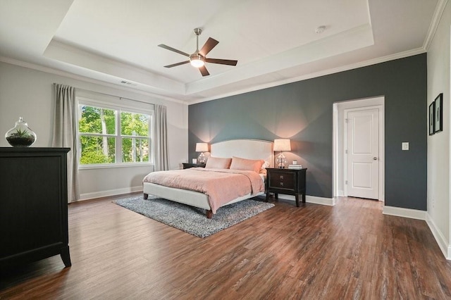 bedroom featuring baseboards, ornamental molding, wood finished floors, and a tray ceiling