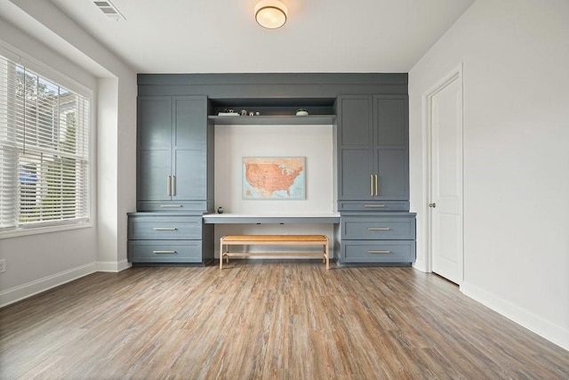 interior space with baseboards, built in desk, wood finished floors, and visible vents