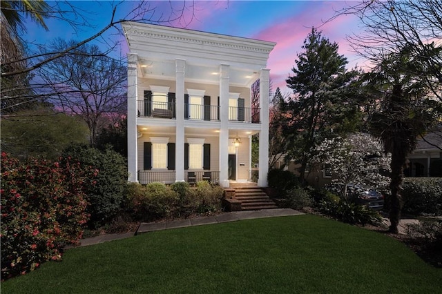 neoclassical home with covered porch, a balcony, and a front lawn