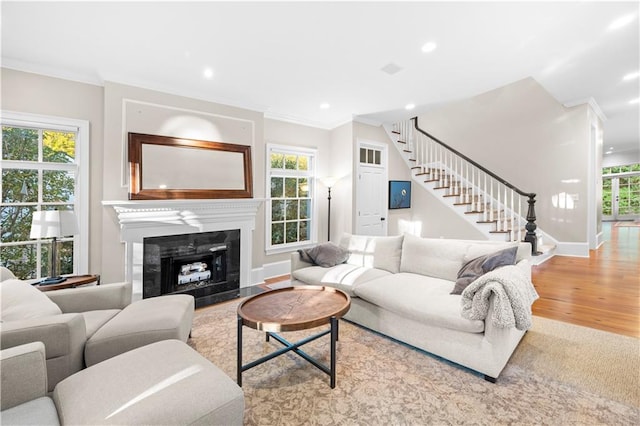 living room with stairs, ornamental molding, wood finished floors, and a fireplace with flush hearth