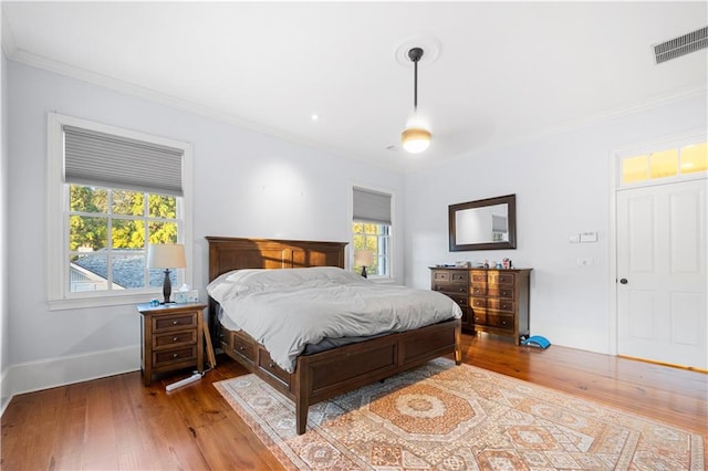 bedroom with baseboards, hardwood / wood-style floors, visible vents, and crown molding