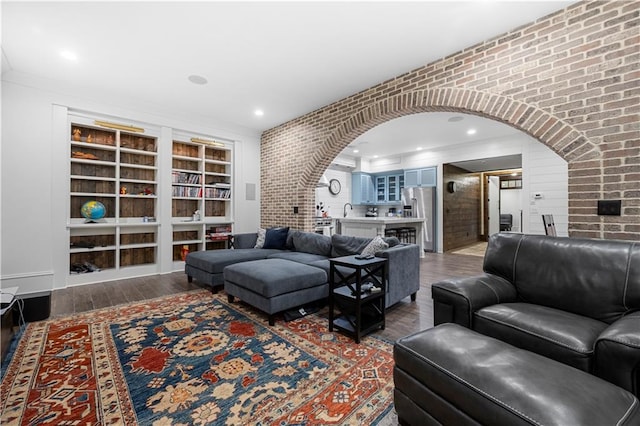 living area featuring brick wall, arched walkways, and wood finished floors