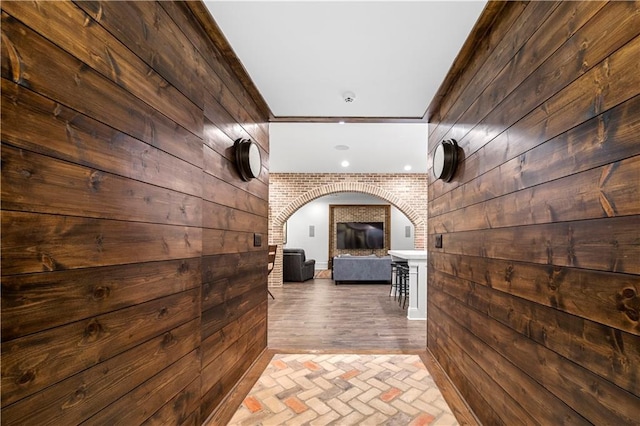 corridor featuring brick floor, arched walkways, and wood walls