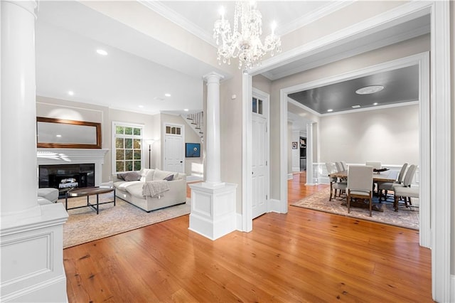 living area featuring light wood-type flooring, ornate columns, ornamental molding, and a glass covered fireplace