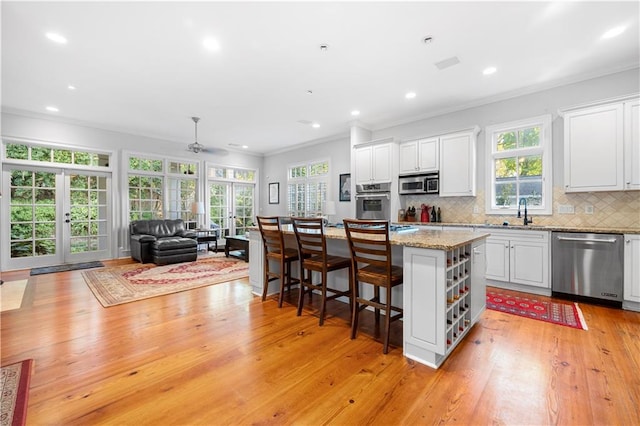 kitchen with a kitchen island, appliances with stainless steel finishes, white cabinets, a kitchen bar, and light stone countertops