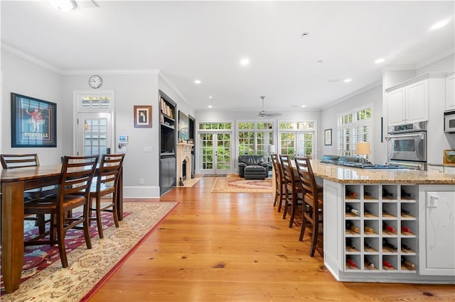 kitchen with ornamental molding, white cabinets, stainless steel oven, and light wood-style flooring