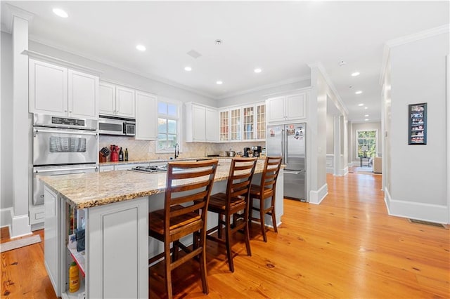 kitchen featuring light wood-style floors, white cabinets, ornamental molding, appliances with stainless steel finishes, and tasteful backsplash