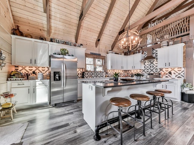 kitchen featuring appliances with stainless steel finishes, white cabinetry, hanging light fixtures, wooden walls, and decorative backsplash