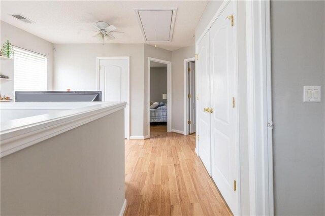 corridor with visible vents, attic access, light wood-style floors, and baseboards