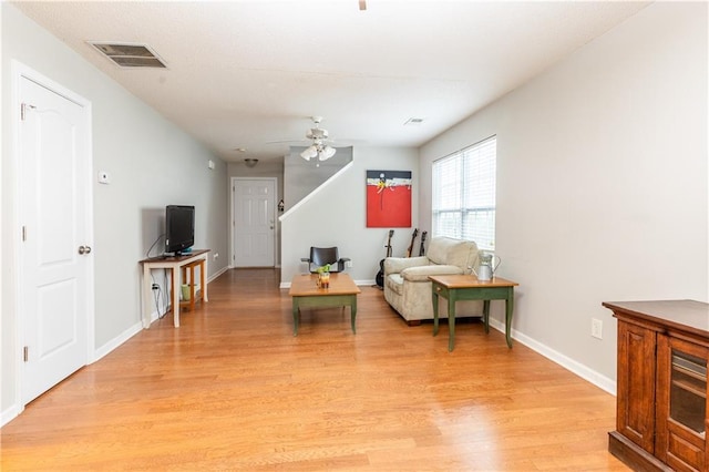 living room featuring ceiling fan, visible vents, baseboards, and light wood-style floors