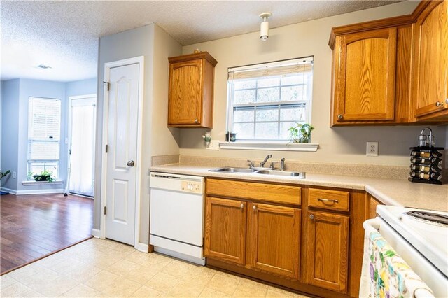 kitchen featuring brown cabinetry, white dishwasher, and a sink