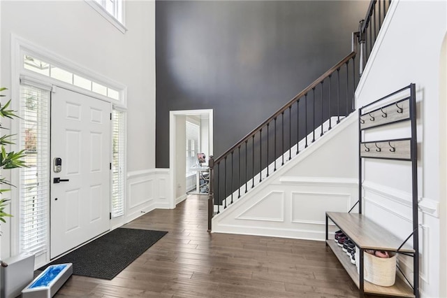 entryway featuring stairs, a decorative wall, wood finished floors, and a towering ceiling