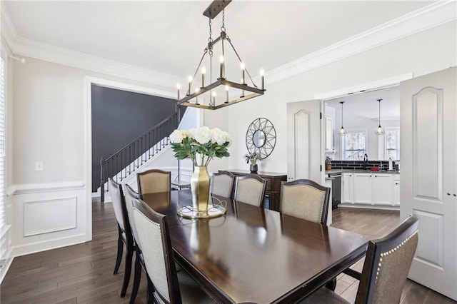 dining space featuring dark wood finished floors, an inviting chandelier, crown molding, a decorative wall, and stairs