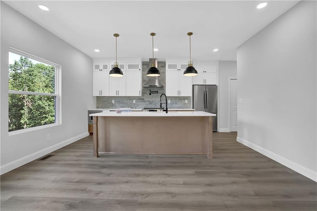 kitchen featuring stainless steel fridge, dark hardwood / wood-style flooring, wall chimney range hood, a center island with sink, and white cabinets