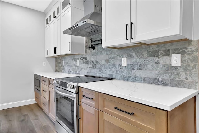 kitchen featuring white cabinetry, stainless steel appliances, wall chimney range hood, light stone counters, and light hardwood / wood-style floors