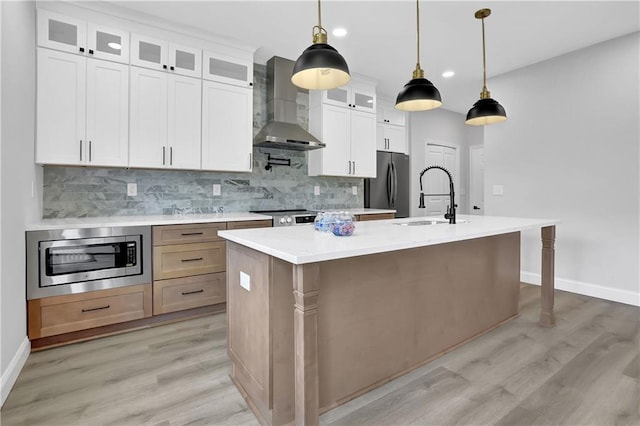 kitchen featuring white cabinets, hanging light fixtures, wall chimney exhaust hood, and an island with sink