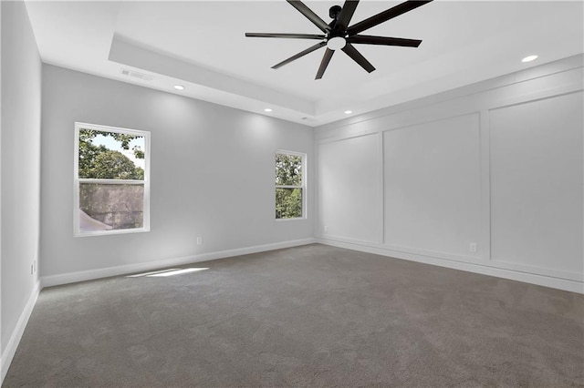 empty room with ceiling fan, carpet floors, and a tray ceiling