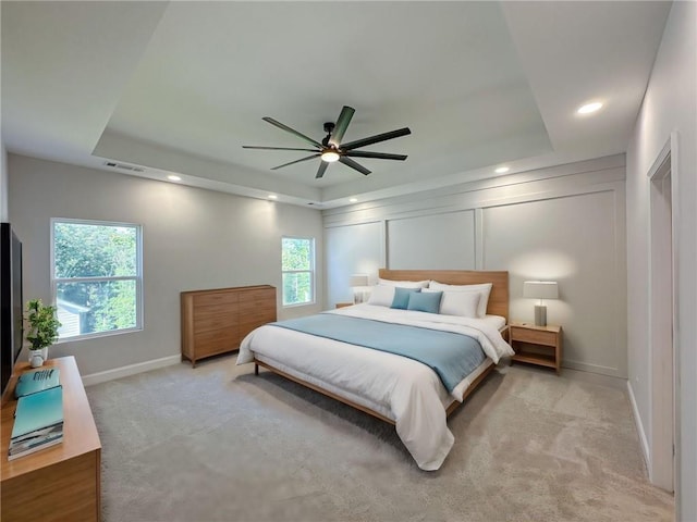 bedroom with a raised ceiling, ceiling fan, and light colored carpet