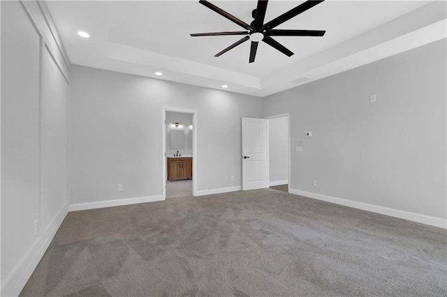 unfurnished bedroom with carpet floors, ensuite bath, a raised ceiling, and ceiling fan