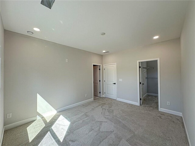 unfurnished bedroom featuring light colored carpet, a walk in closet, and a closet