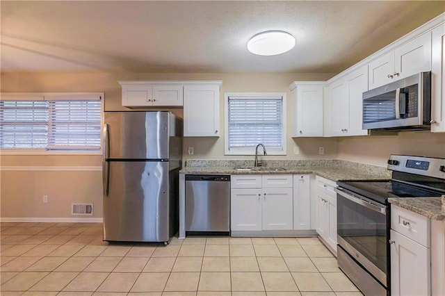 kitchen featuring light stone countertops, sink, stainless steel appliances, white cabinets, and light tile patterned flooring