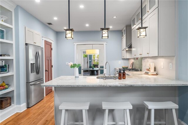 kitchen with light stone counters, a sink, stainless steel fridge with ice dispenser, light wood-style floors, and a peninsula