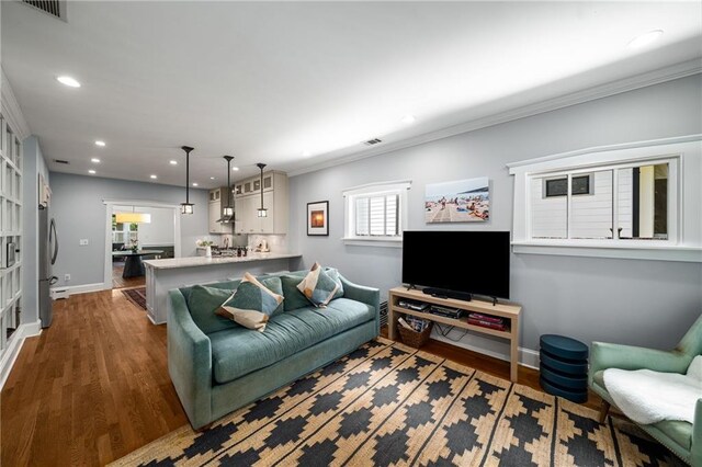 living room featuring visible vents, wood finished floors, baseboards, ornamental molding, and recessed lighting