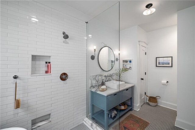 full bath with baseboards, a tile shower, and vanity