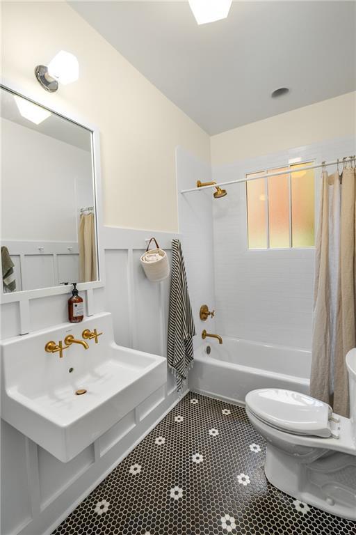 full bathroom featuring tile patterned flooring, wainscoting, shower / tub combo, toilet, and a decorative wall